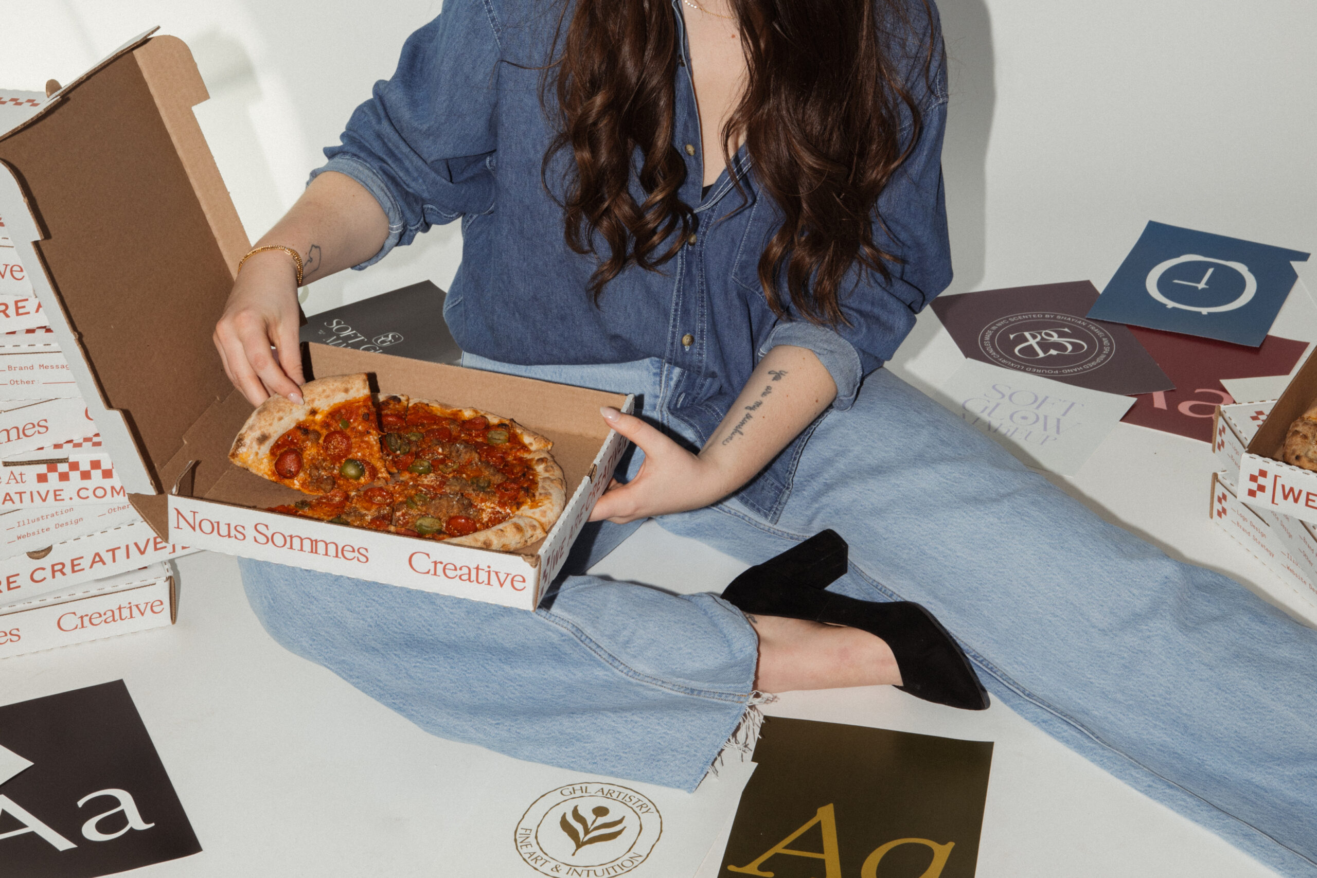 Branding designer grabbing pizza from a branded pizza box with scattered logos all around