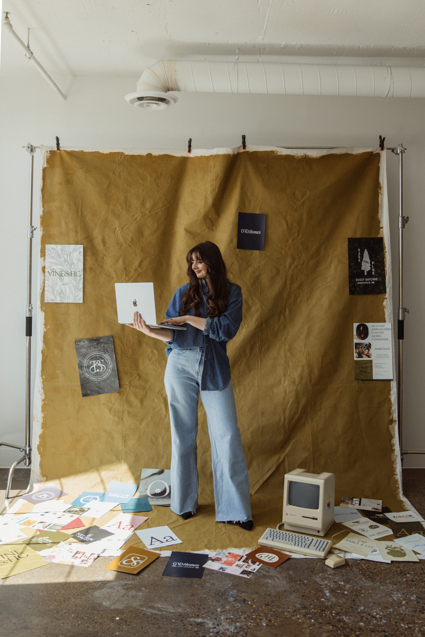 Brand designer holding a computer surrounded by work from previous branding kits